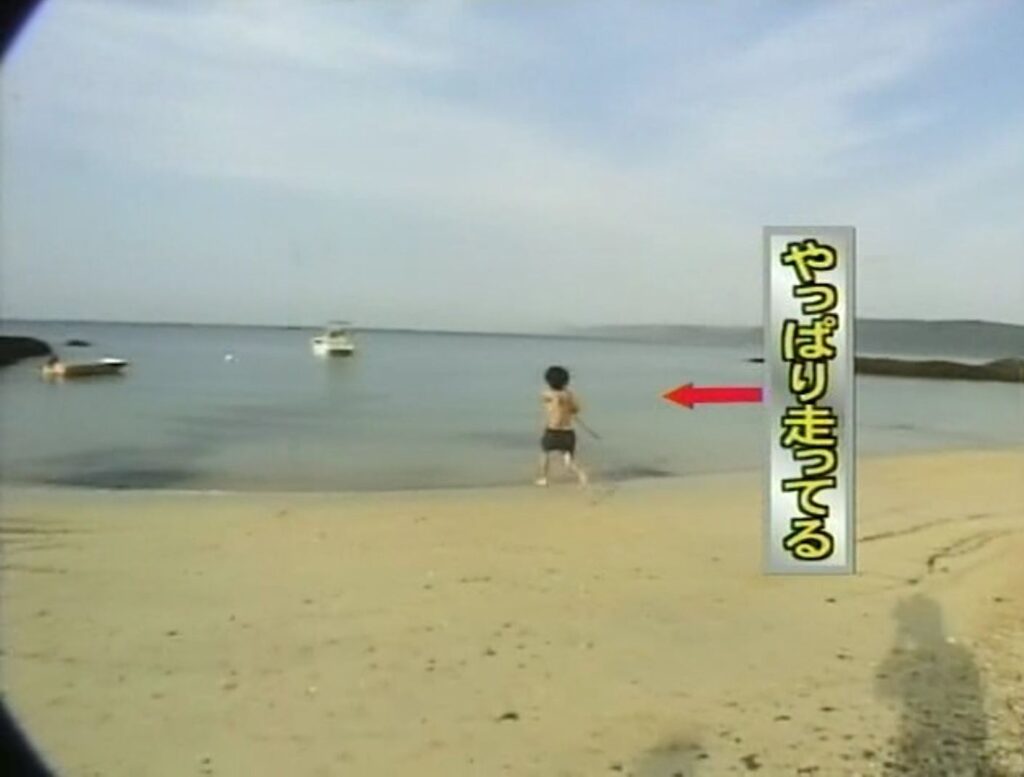 海パン一丁で木製のヤリを持って砂浜を走る大泉さん